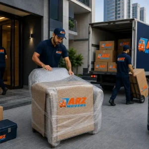 ARZ Movers team in blue uniforms loading furniture and boxes with branded truck outside a modern apartment tower.